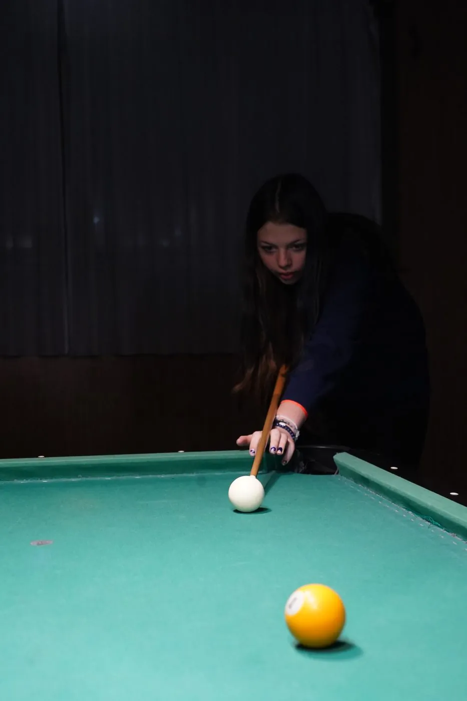 Žena hraje kulečník v šeru herny