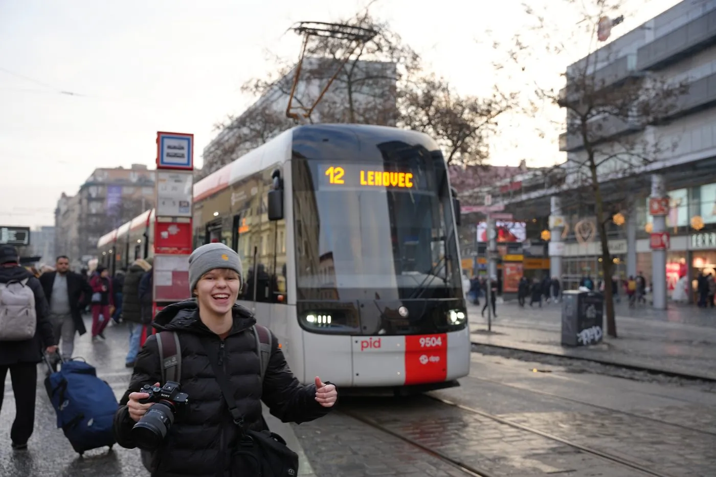 Usměvavý fotograf s foťákem u tramvajové zastávky